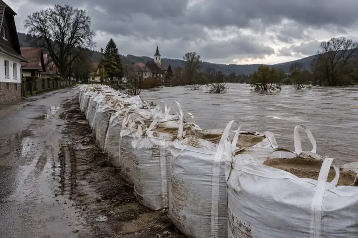 Row of sand-filled bulk bags forming a temporary flood barrier along a swollen river