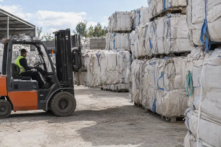 Bales of used white woven bulk bags stacked in a recycling yard with a forklift